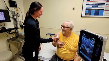 Med student using ultrasound on man's shoulder in medical exam room