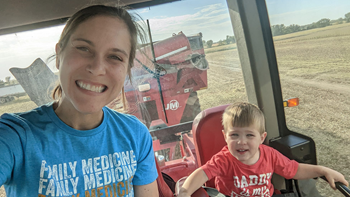 A mother smiles for a selfie with her toddler son in a tractor.