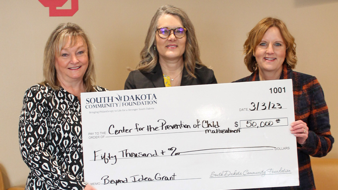 Three people stand and hold a big check for $50,000 made out to the Center for the Prevention of Child Maltreatment from the South Dakota Community Foundation.