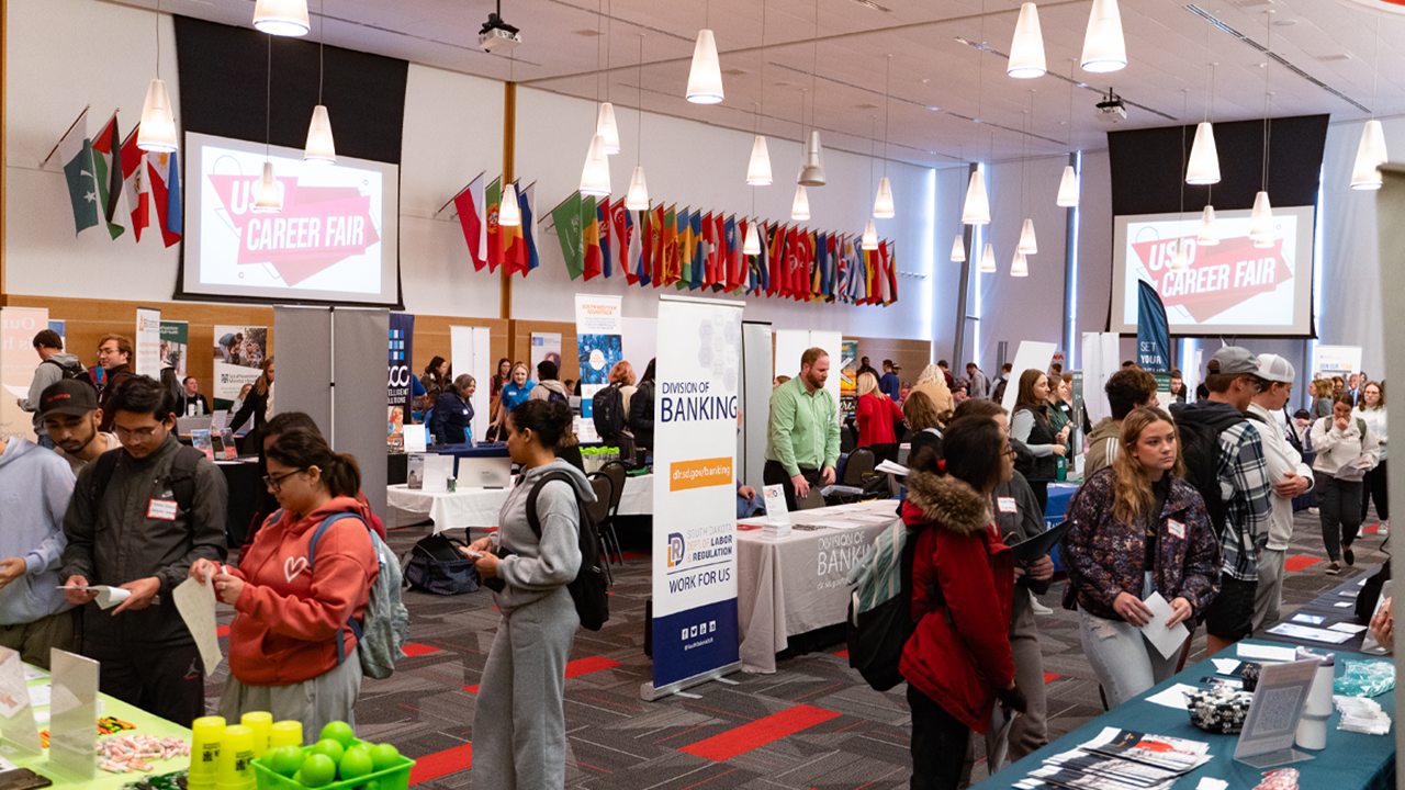 A busy room full of employer booths and tables and students walking around.