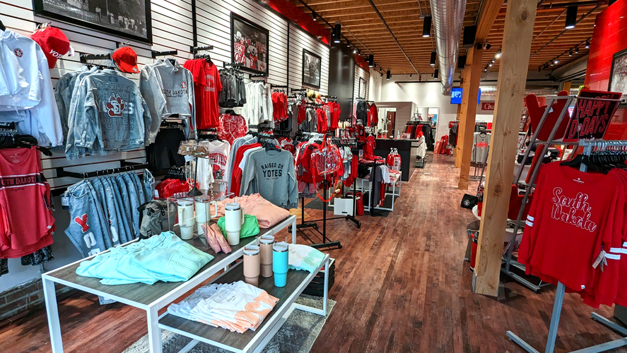 A look inside the Charlie's store in downtown Vermillion. Red USD apparel hangs on clothing racks, and jeans, sweatshirts and jackets hang on racks on the wall.