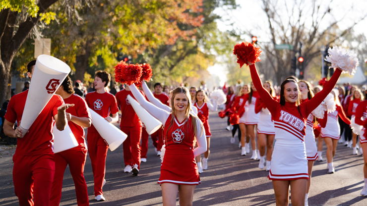 Cheerleaders dressed in red and white cheer and smile as they walk down Vermillion's Main Street in the fall.