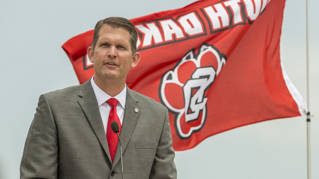 David Herbster behind a lectern talking to a crowd. Behind him the USD flag blows in the wind. David Herbster behind a lectern talking to a crowd. Behind him the USD flag blows in the wind.