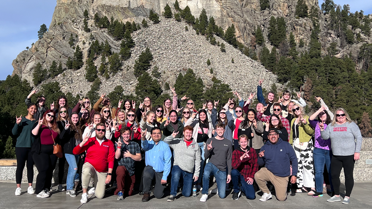 A large group of students poses for a photo in front of Mount Rushmore.