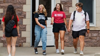 Students walking from Old Main Three students walk out the doors of Old Main, waving and smiling to students who are walking in. They are all wearing Charlie's gear.