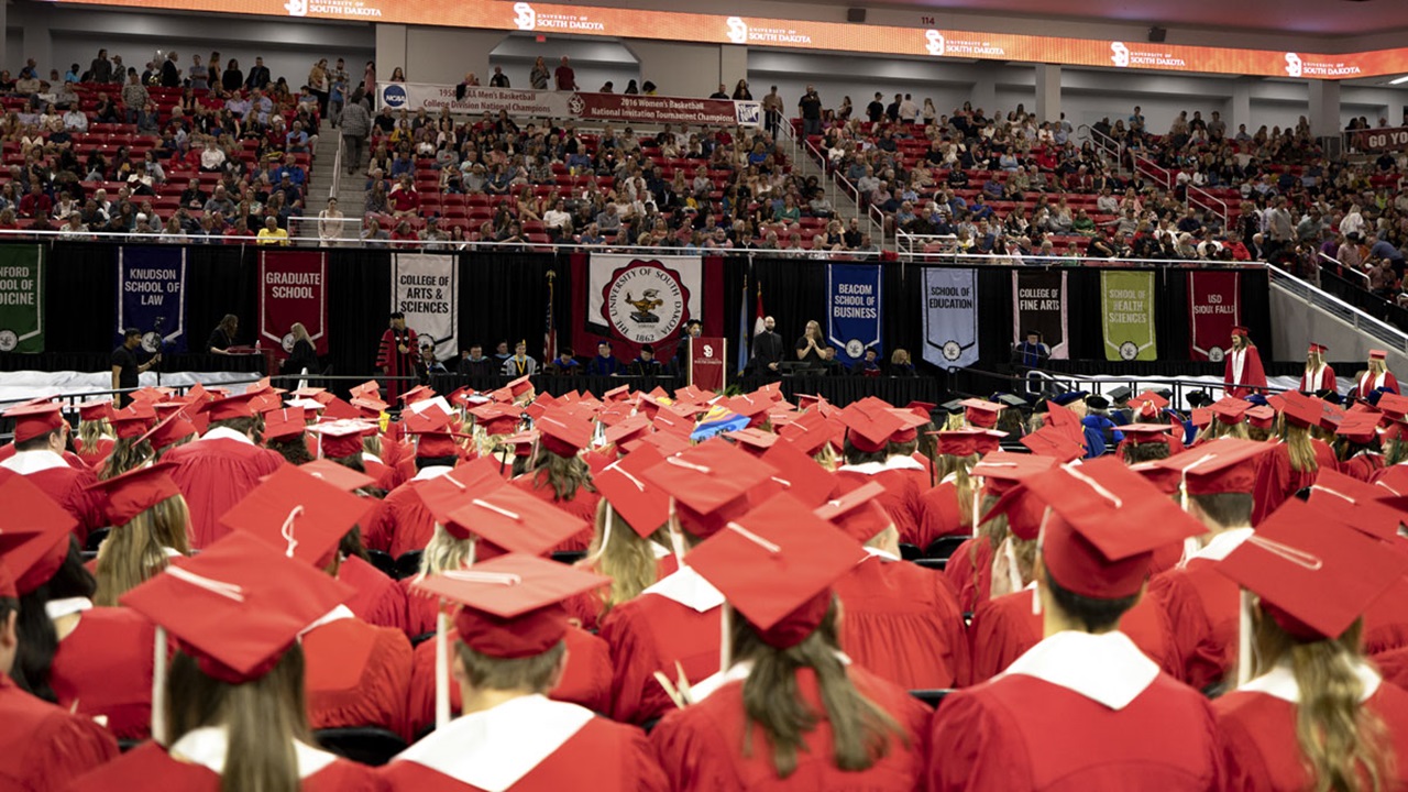 USD Class of 2023 graduates sit together in caps and gowns. USD Class of 2023 graduates sit together in caps and gowns.