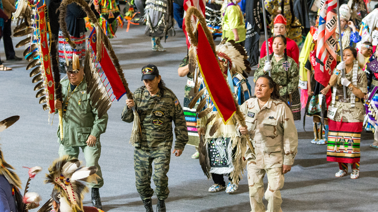 Native alumni and veterans celebrate the annual Wacipi at the University of South Dakota. They dress in cultural uniforms and carry flags.