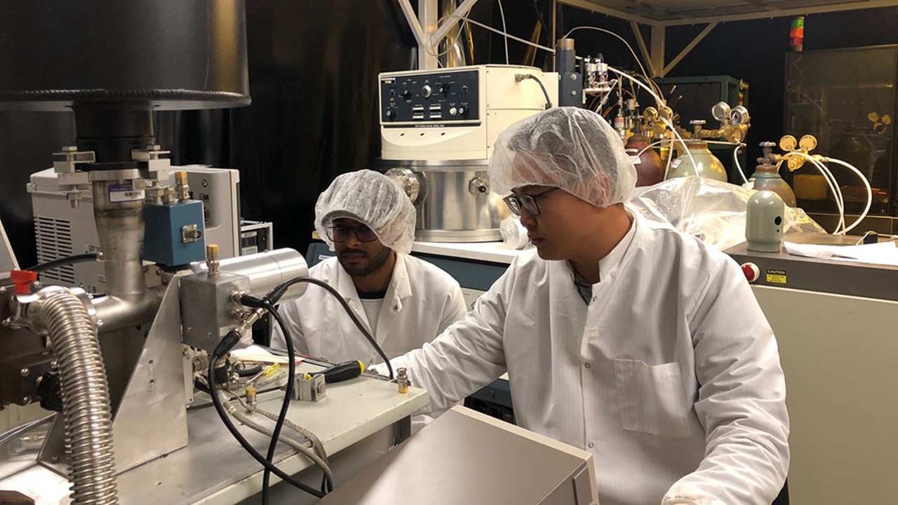 Two students work with scientific equipment inside a laboratory.