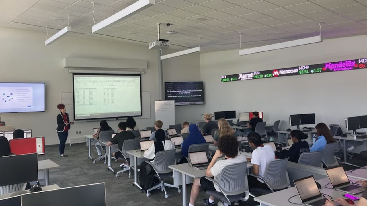 High school students sit in desks as a Beacom School of Business professor lectures at the front of the room. High school students sit in desks as a Beacom School of Business professor lectures at the front of the room.