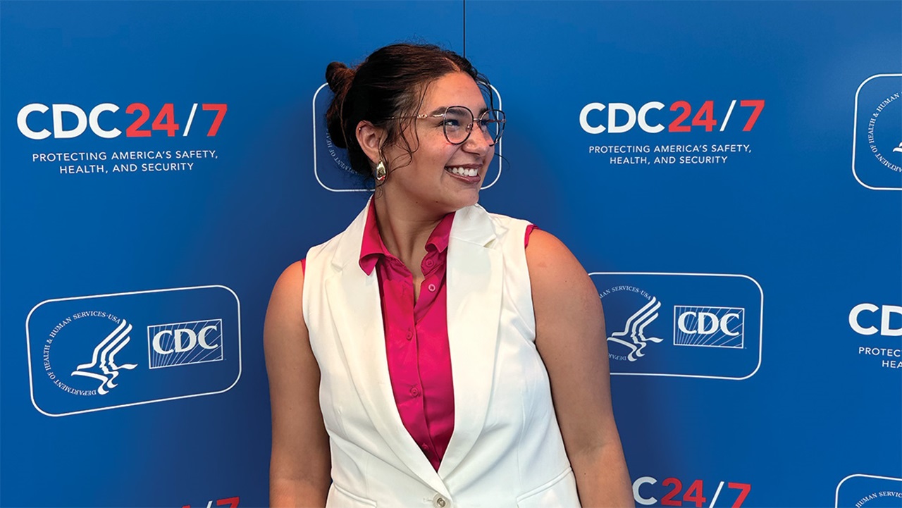 Zena Aragon stands in front of a wall decorated with CDC logos and slogans.