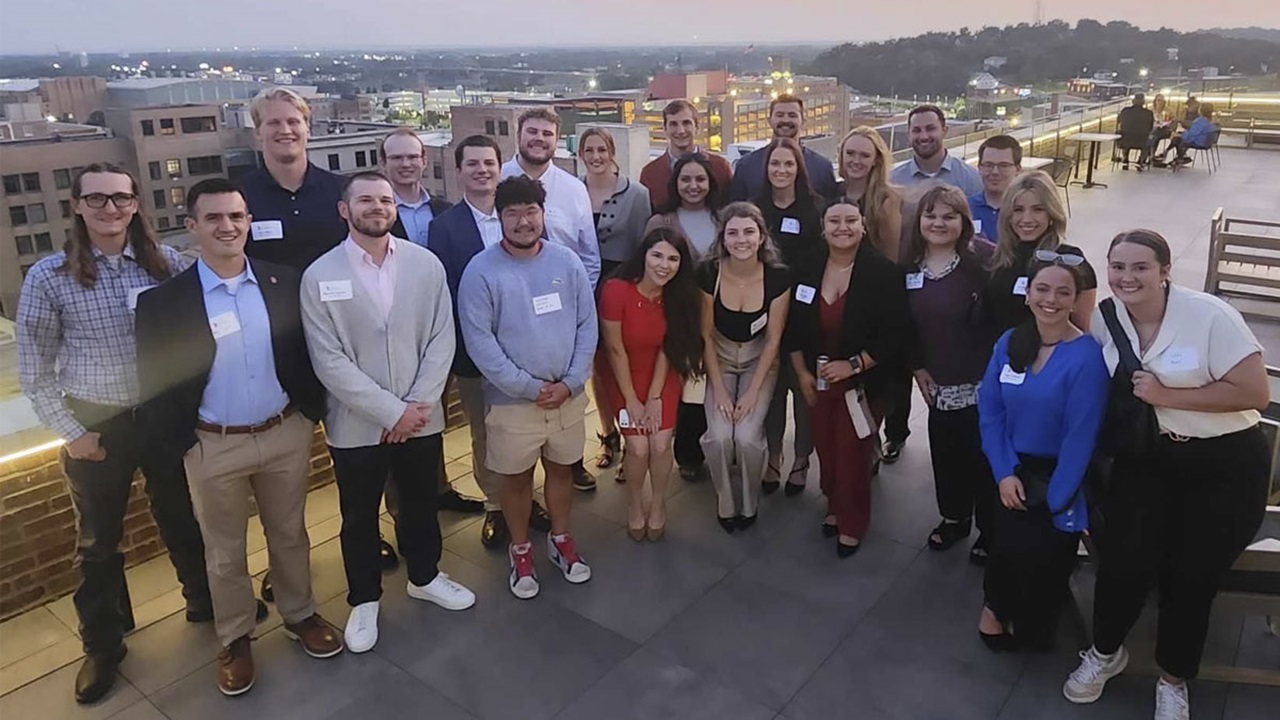 Sioux City Night 2024 A diverse group of law students pose at dusk for a photo on a rooftop terrace with city lights in the background.