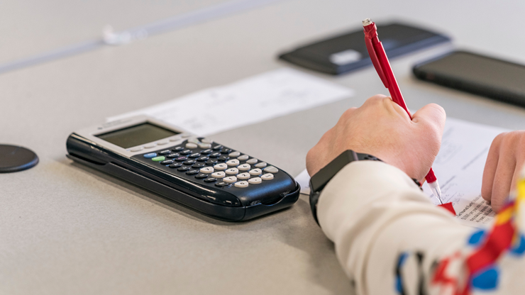 A person concentrating on writing down numbers on a piece of paper, while using a TI-84 Plus graphing calculator for reference.