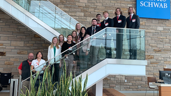 Business students stand beside each other going up a staircase in a Charles Schwab building.