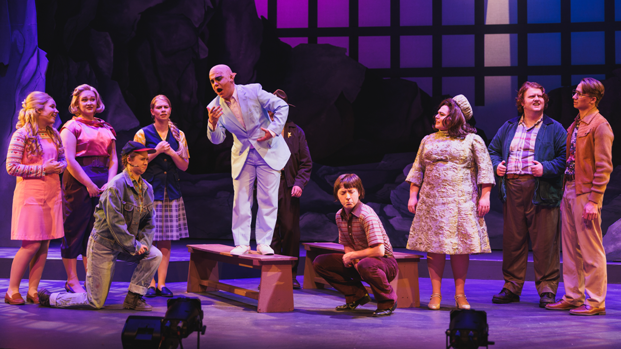 Several actors and actresses act out a scene on stage.