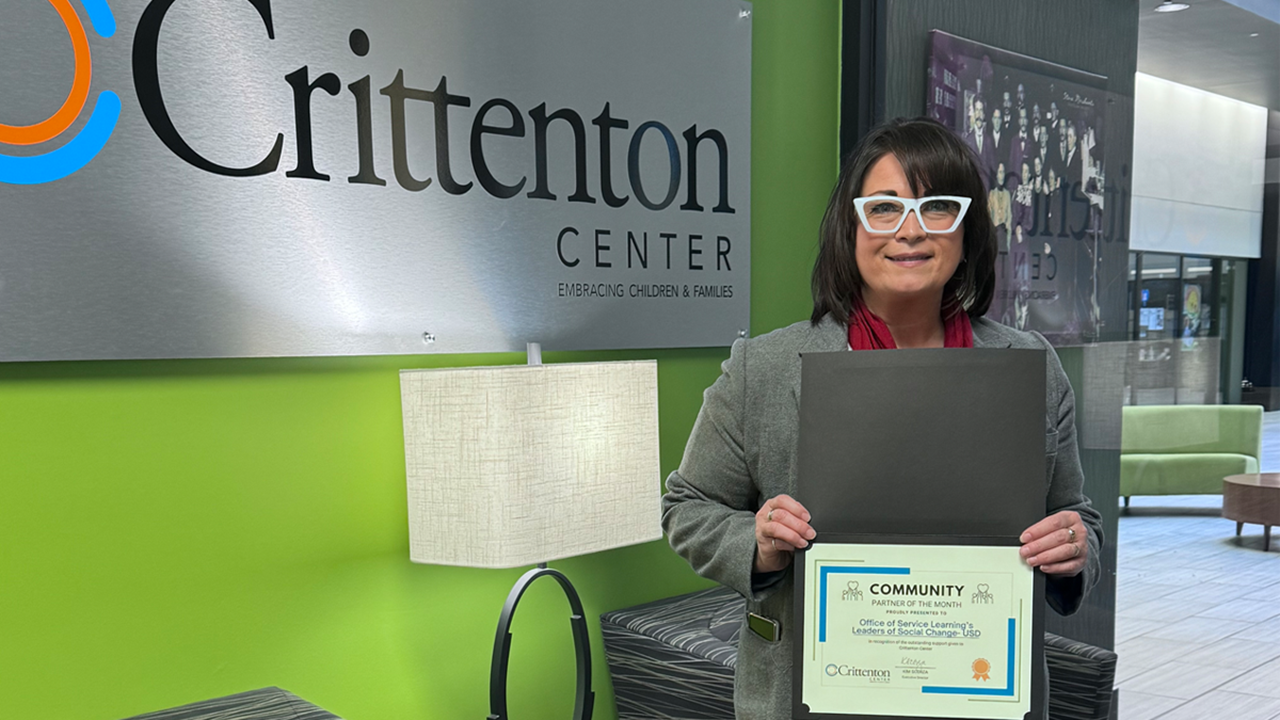 April Lee smiles and holds an award certificate in front of a sign that says Crittenton Center.