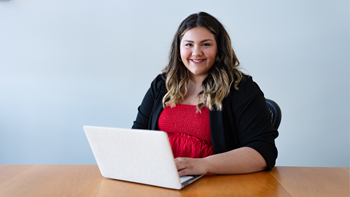 Ellen Mallory sits at a table and smiles with her laptop opened in front of her.