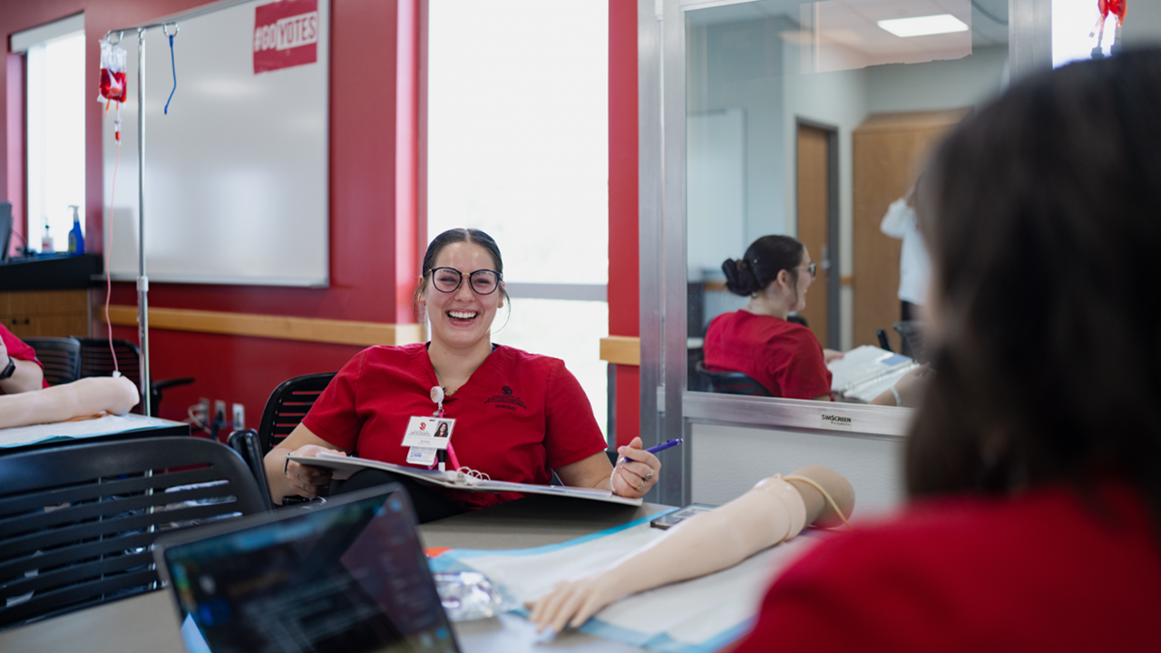 Nursing students in scrubs study at a table.