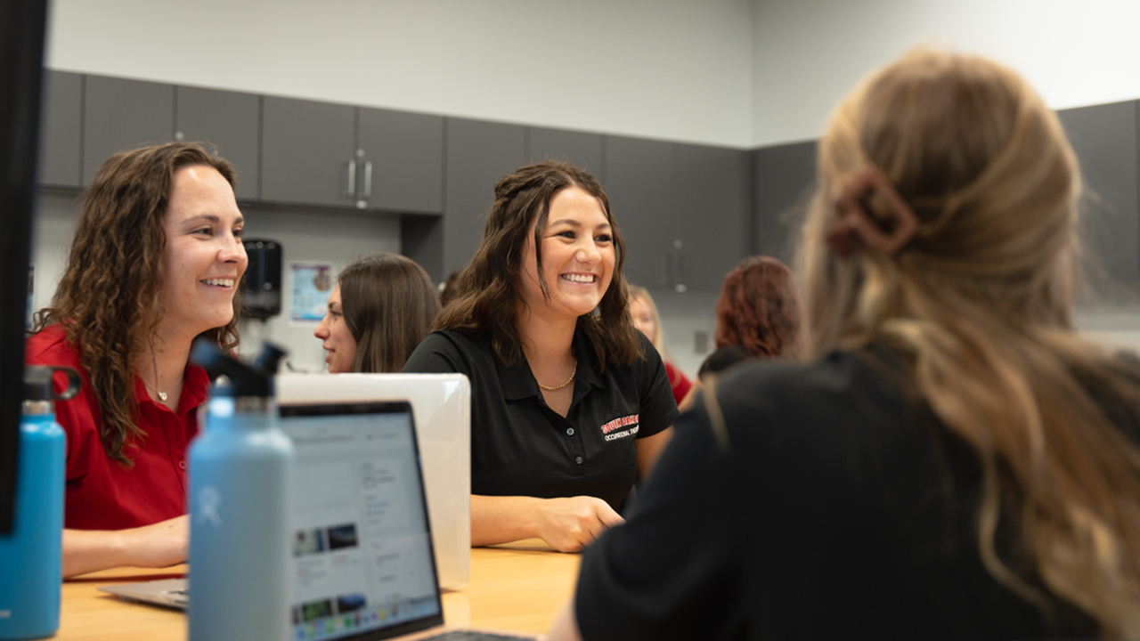 Occupational therapy students sit at a table, talking and smiling.