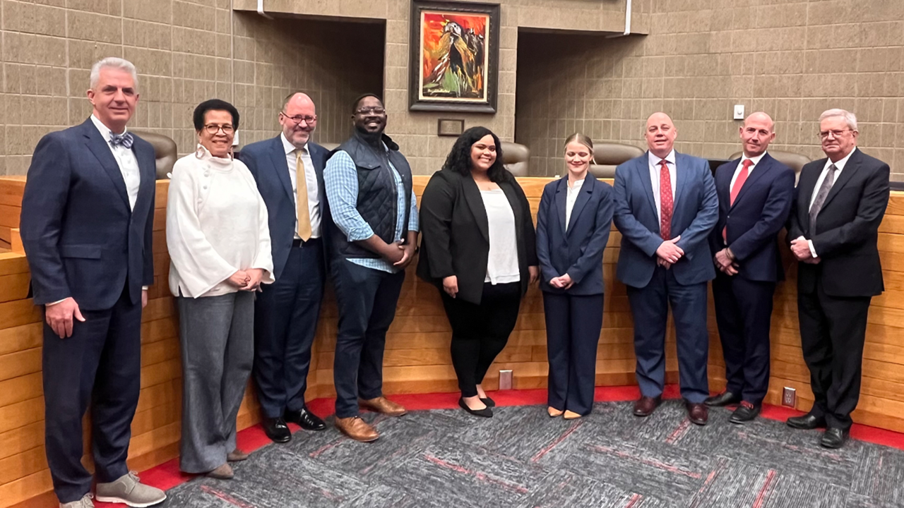 Nine law professionals stand together for a photo in the courtroom.
