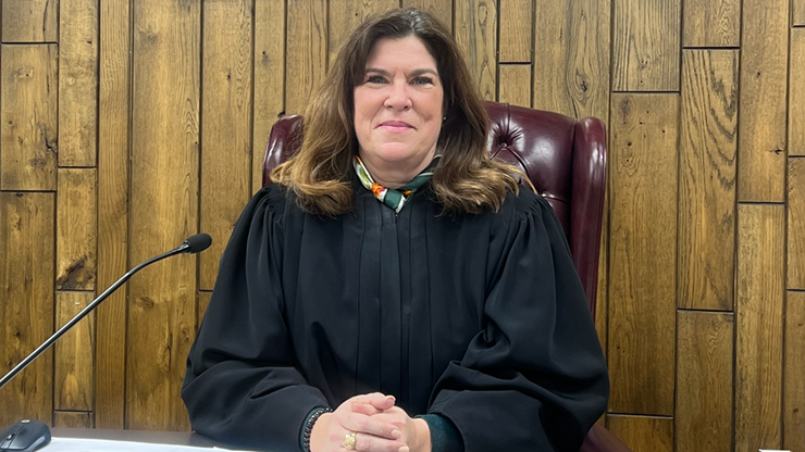 Julie Dvorak wears a judge gown and sits with her hands together on the desk in front of her.