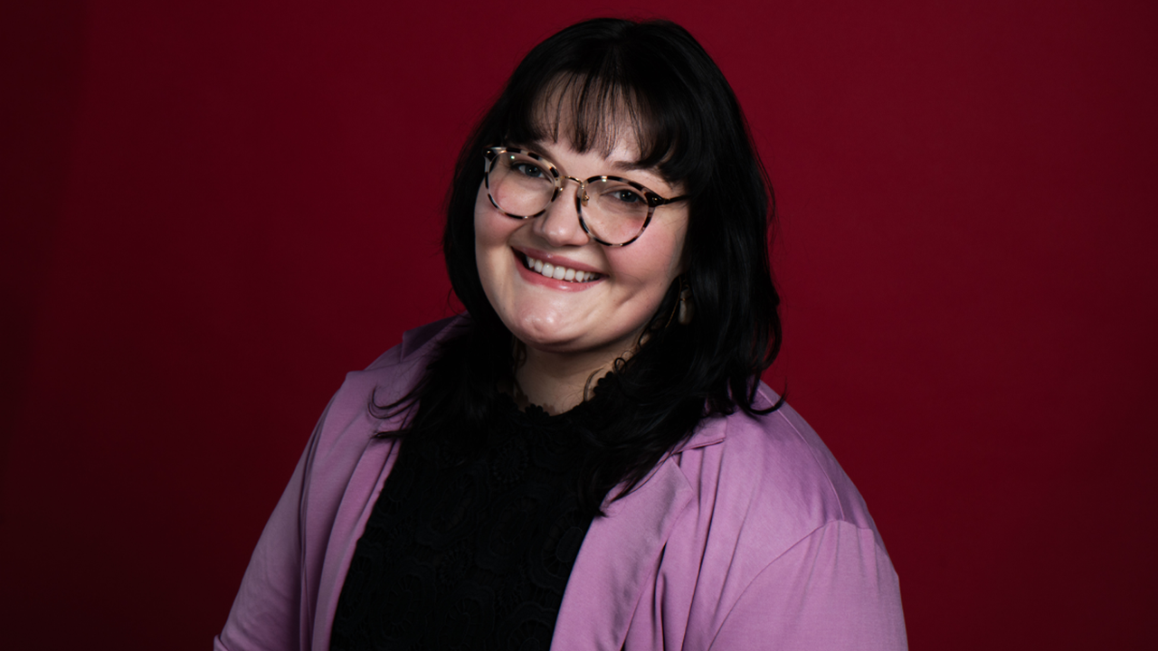 A professional headshot of Abigail Ruda against a dark red background.