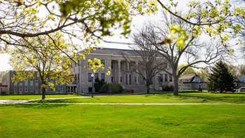The College of Arts & Sciences exterior, with a sunny, green campus surrounding it.