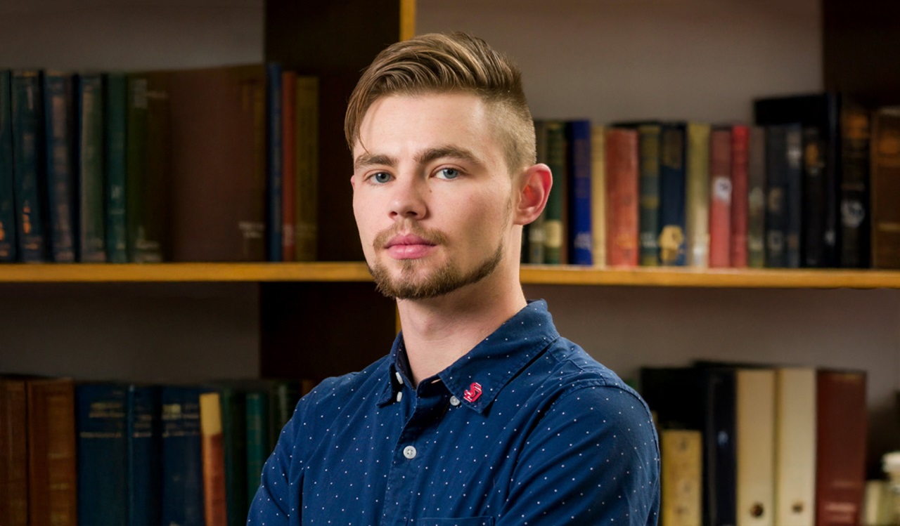 USD doctoral student Casey Wall faces the camera and poses for a picture in a blue shirt.