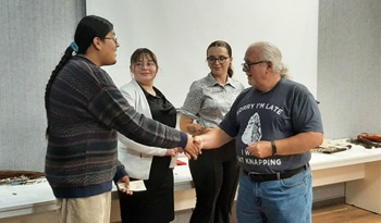 The 2025 Justin Runestad Scholarship recipients stand in a line to receive their award, as Angel Vazquez shakes the hand of a gentleman giving him the award.