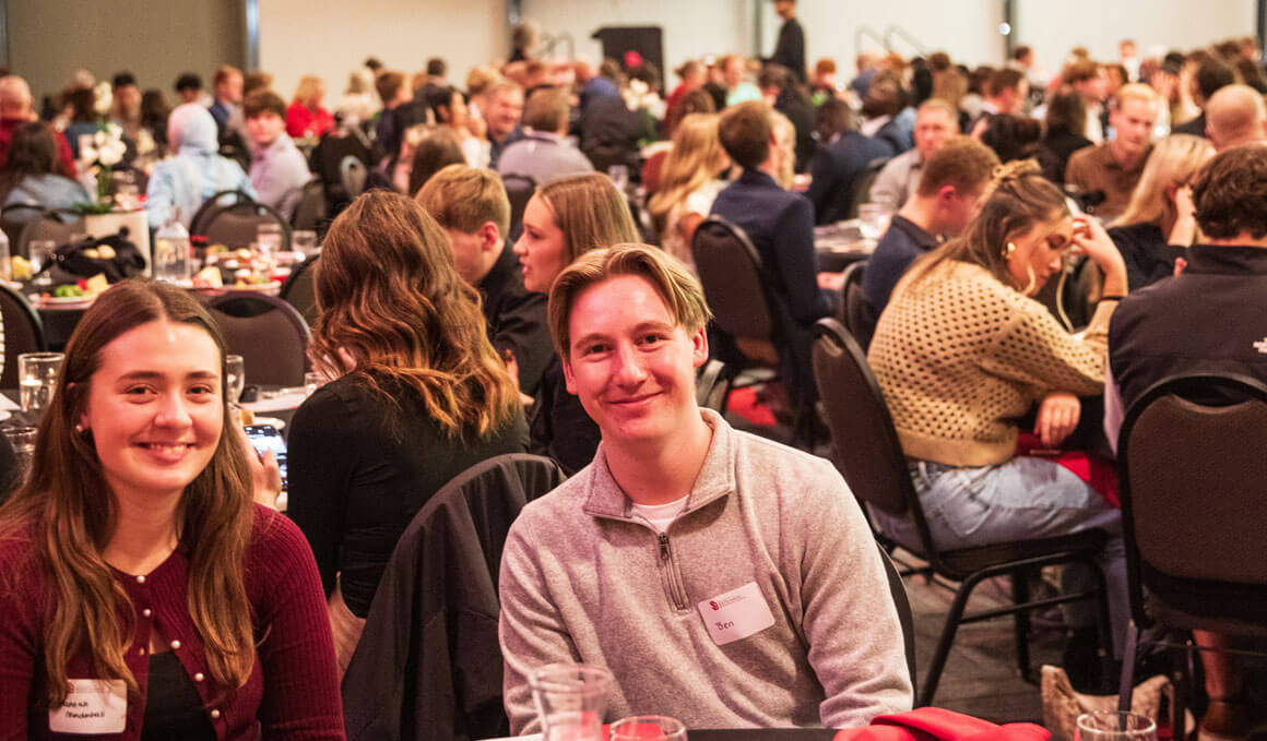 Students, staff and faculty of the Beacom School of Business gather at large banquet hall, seated at round tables, with two smiling attendees in the foreground looking toward the camera.
