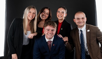 Katie Gellerman poses with other USD students, in professional attire, against a black backdrop.