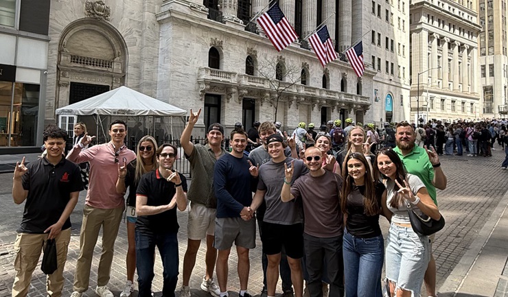 Students from the USD Beacom School of Business' Financial Management Association and the President's Student Leadership Institute stand on Wall Street in New York City, making the Coyote sign with their hands.