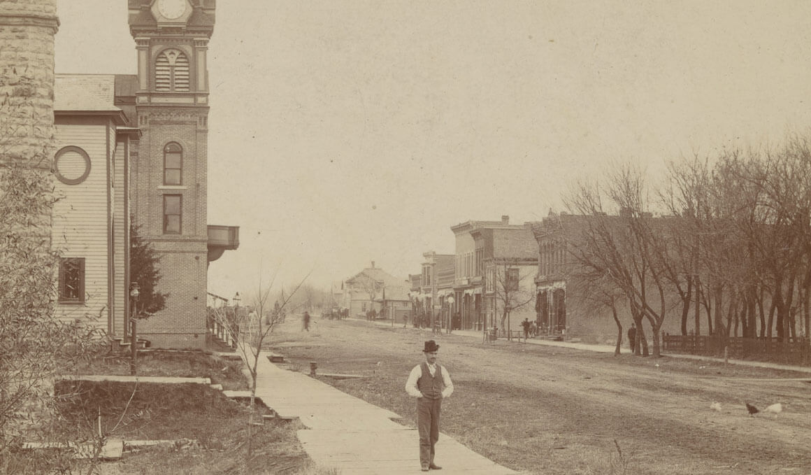 Main Street looking west, with a man, possibly R. Z. Shriner, on the boardwalk and a view of the First Baptist Church and City Hall, undated, approximately 1889-1896.
