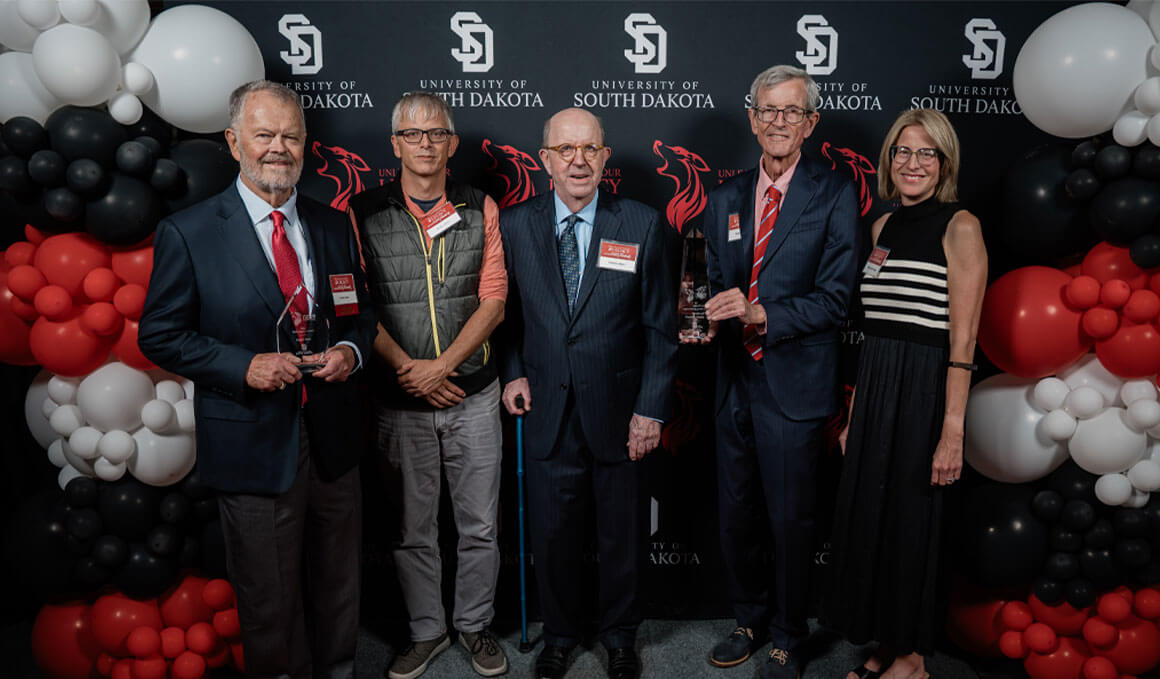 Unleash Your Legacy winners stand together in front of a black backdrop with the USD logo, flanked by red, white and black balloons.