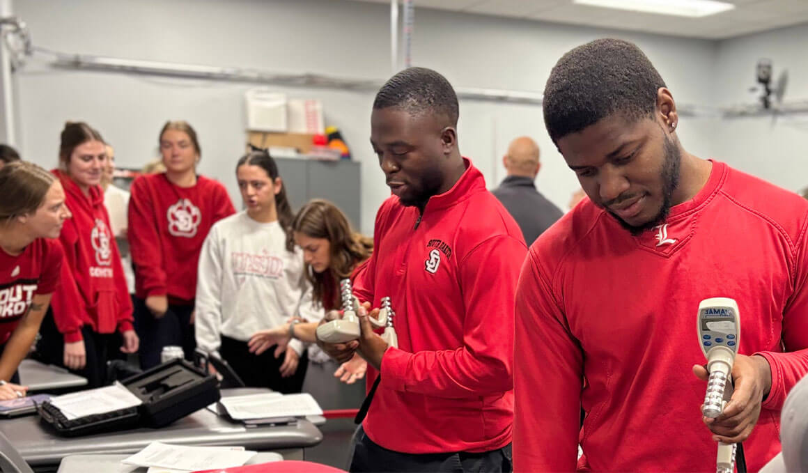 USD students stand in Coyote red attire, reviewing the upgraded KSM equipment.