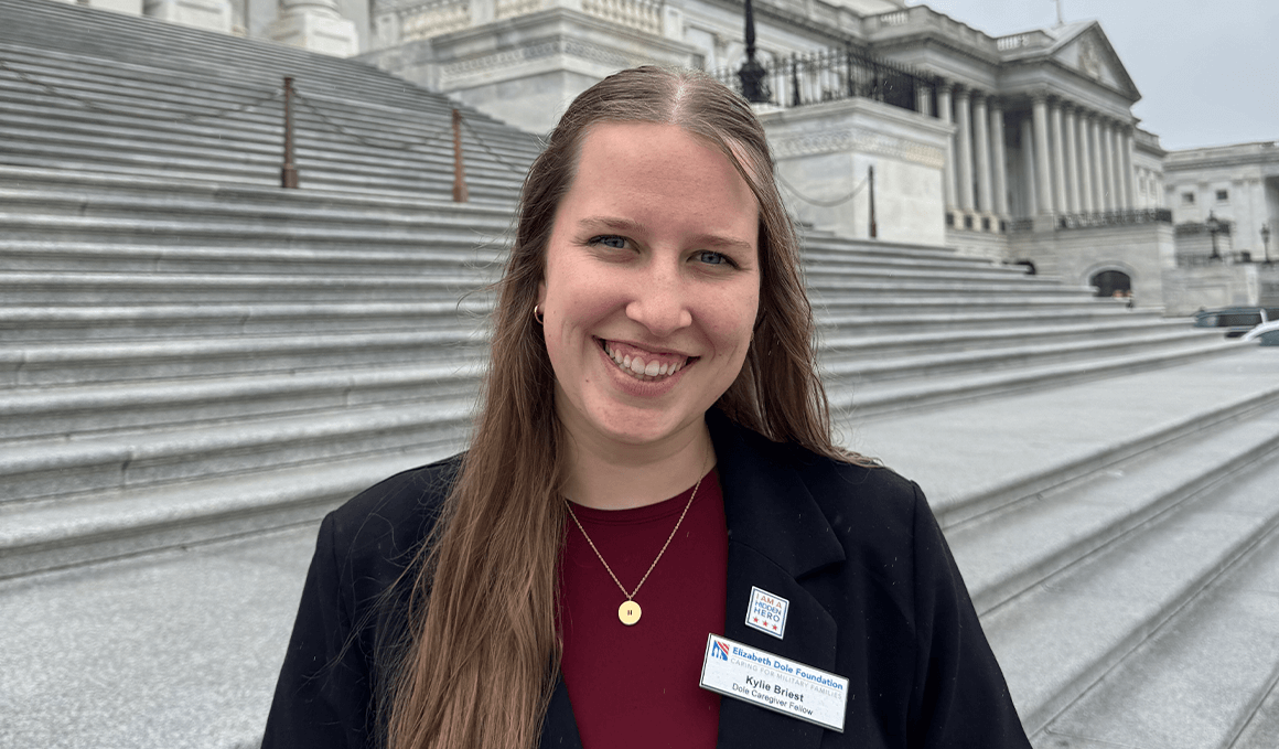 Kylie Briest, wearing a dark blazer over a maroon shirt, smiles directly at the camera while standing on the wide stone steps leading up to the U.S. Capitol Building.