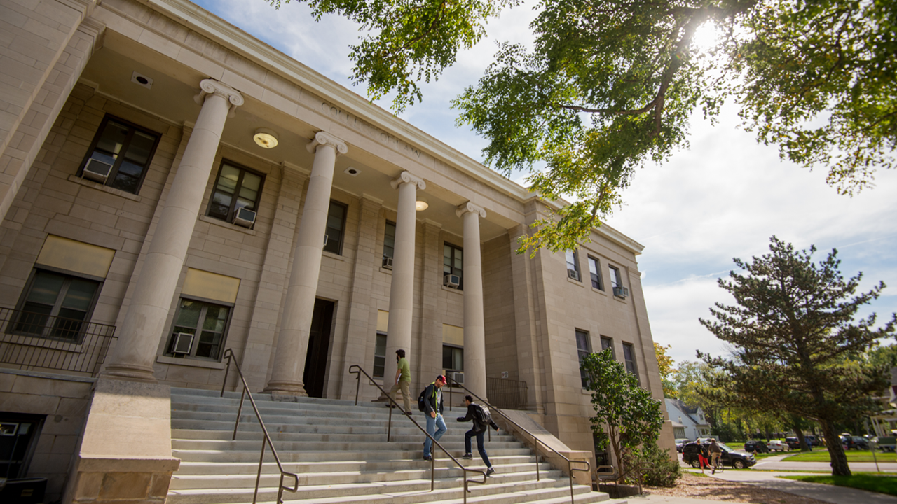 Students and faculty walk into and out of the the exterior front of the College of Arts and Sciences.