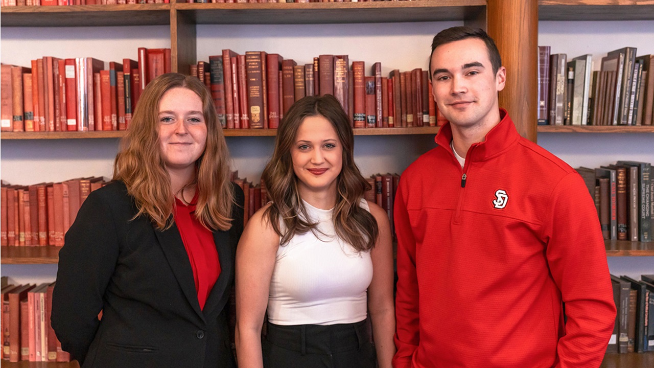Waverly Patterson, Julia Stanek and Max Mickelson stand together in a library of colorful books. Waverly Patterson, Julia Stanek and Max Mickelson stand together in a library of colorful books.