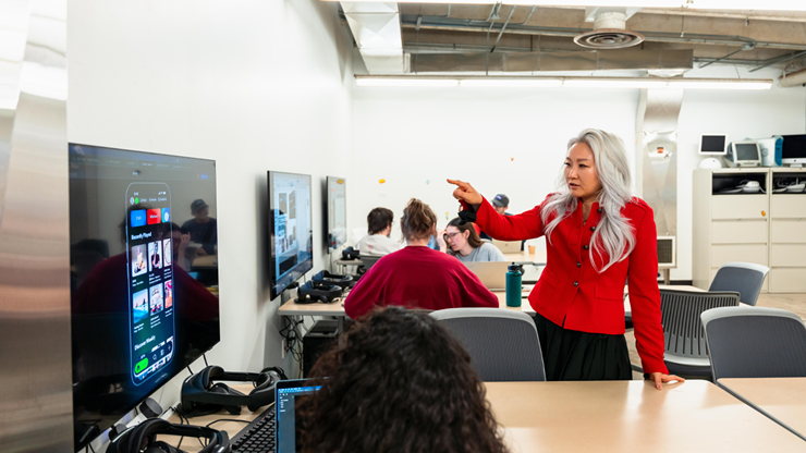 USD's Young Ae Kim, Ph.d, points to a T.V. screen and instructs a student in the classroom.