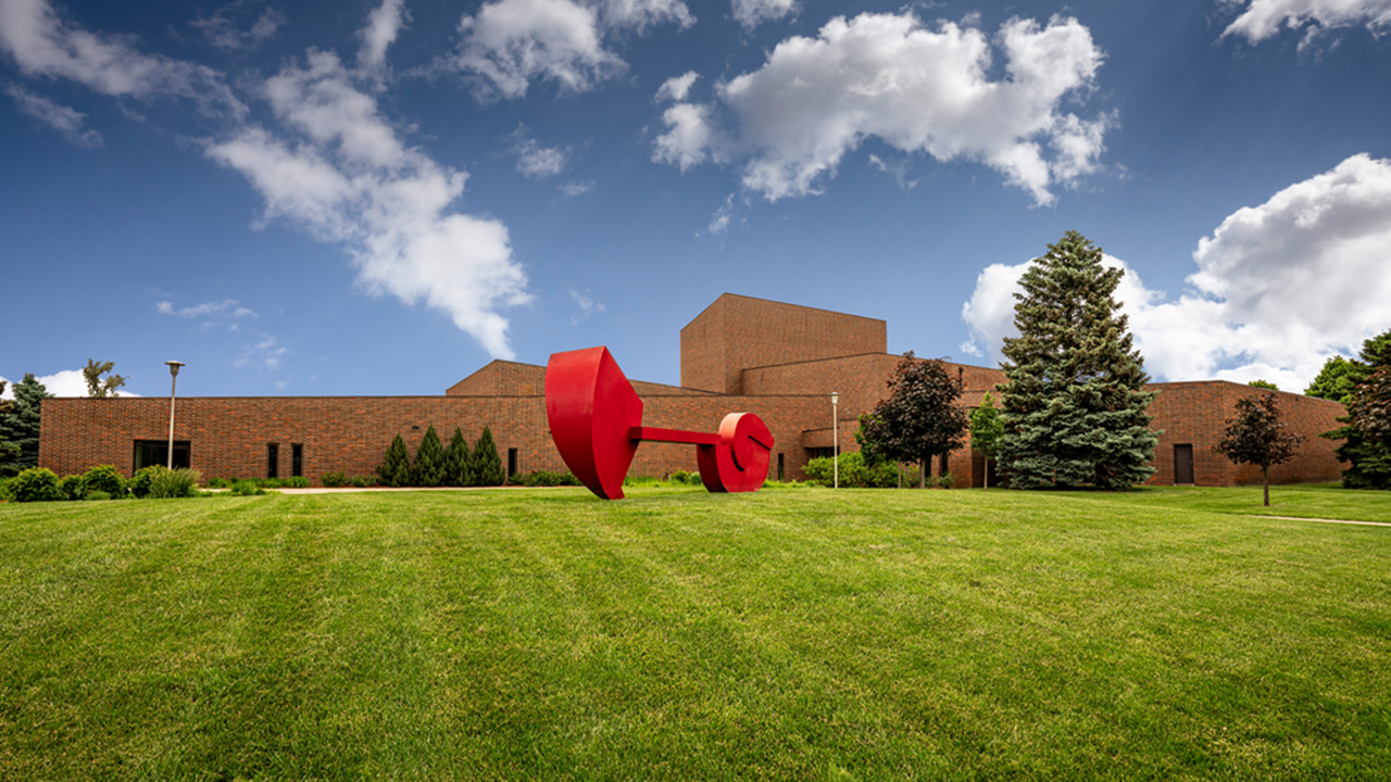 The exterior of the Warren M. Lee Center for Fine Arts sits on the University of South Dakota campus with a blue sky and white clouds in the background.