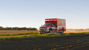 An red and white ambulance speeds down a dirt road.