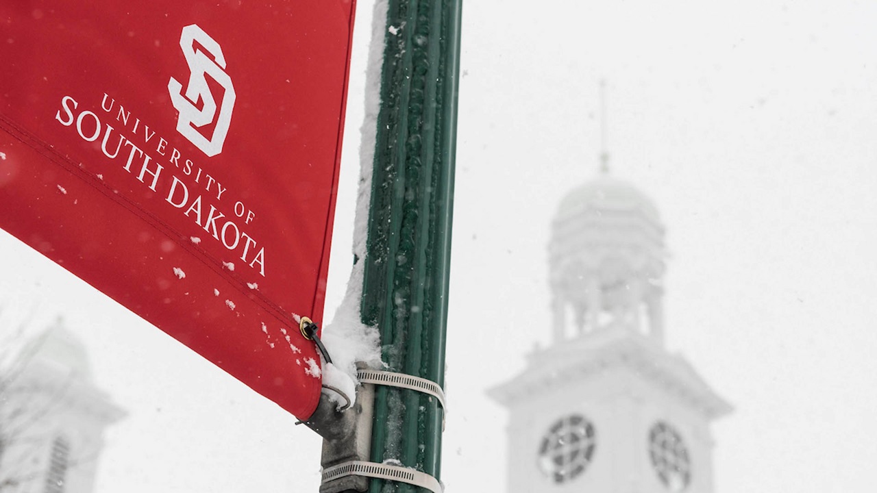 USD banner on the snowy campus with a building in the background.