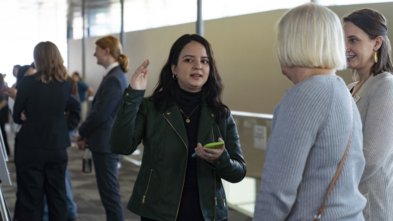 USD student Mariana Astete talks to two community members, explaining her research poster at IdeaFest. USD student Mariana Astete talks to two community members, explaining her research poster at IdeaFest.