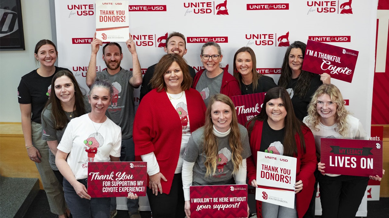 A group of people standing together holding a variety of alumni signs for Unite for USD. A group of people standing together holding a variety of alumni signs for Unite for USD.