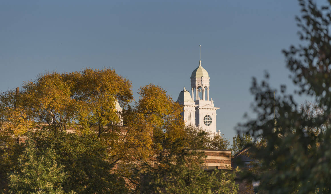Old Main's tower can be seen peering through tree-tops that hold fall colors. 