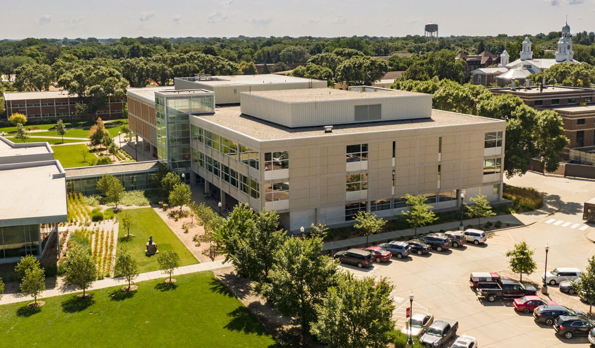 A drone photo of the I.D. Weeks Library exterior. Surrounding it are other USD campus buildings, green grass, and a parking lot to the right of the library.