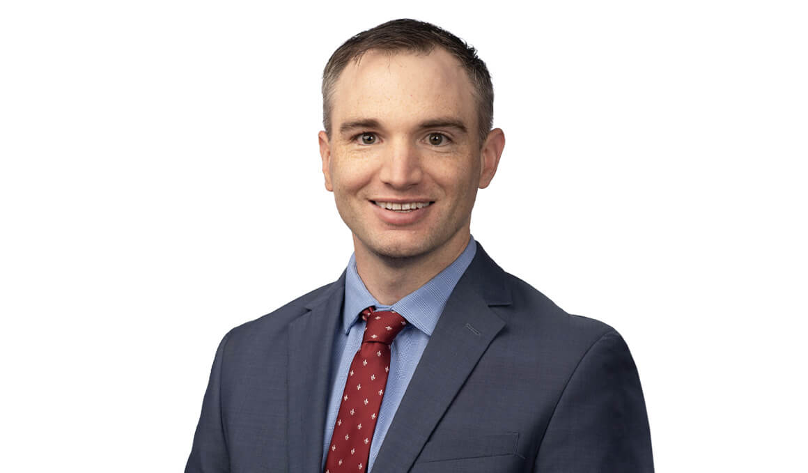 Ben Meyerink, M.D., sits for his professional photo against a white background. He is wearing a dark blue suit with a red tie and smiling at the camera.