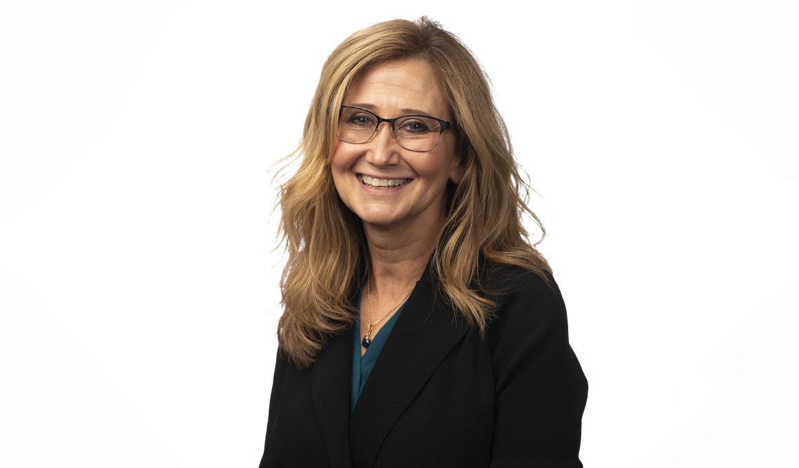 Michelle Baack, M.D., sits against a white backdrop and poses for her professional photo. She is wearing a dark blue outfit, glasses and smiling at the camera.