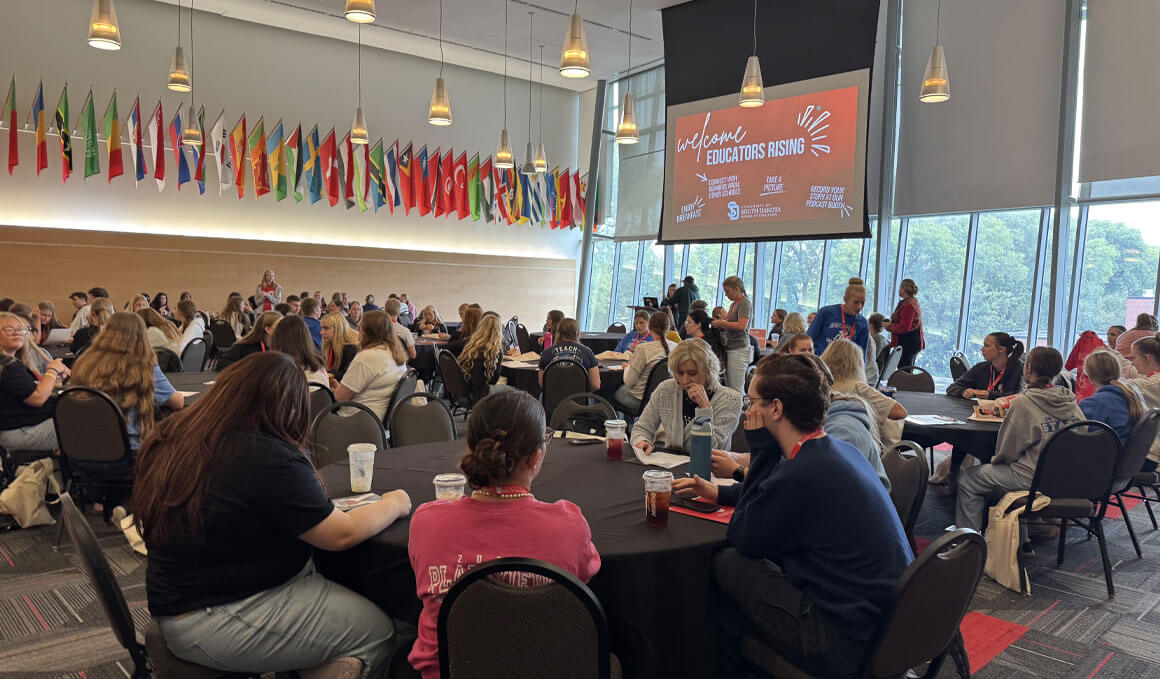 Participants of the 2026 Educators Rising Day sit at round tables, in the Muenster Center ballroom, as they converse with each other.