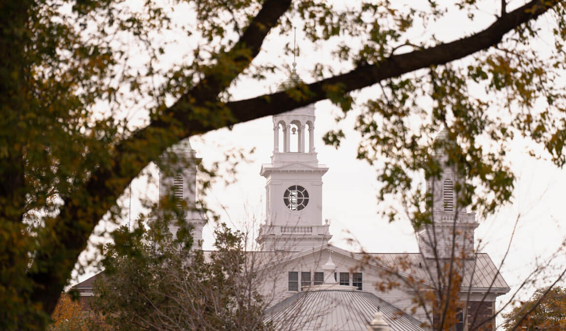 A close-up of Old Main's bell tower, seen through the limbs of a tree that is beginning to lose its leafs for the fall season.
