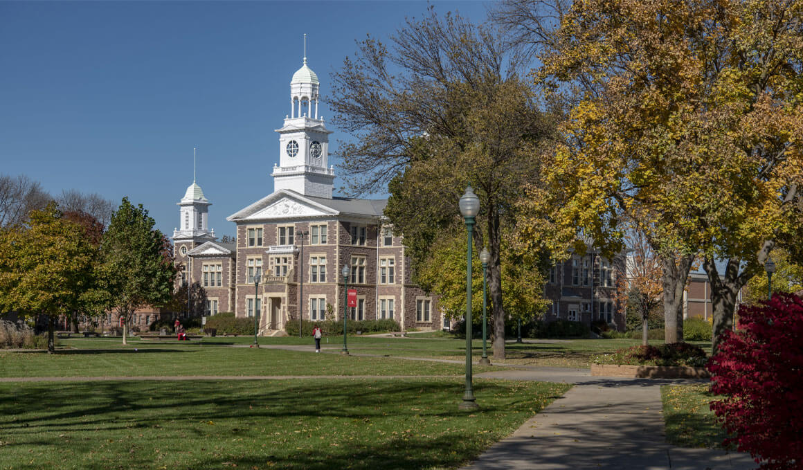 USD's historic Old Main stands beyond a broad green lawn, framed by autumn trees and a walking path.